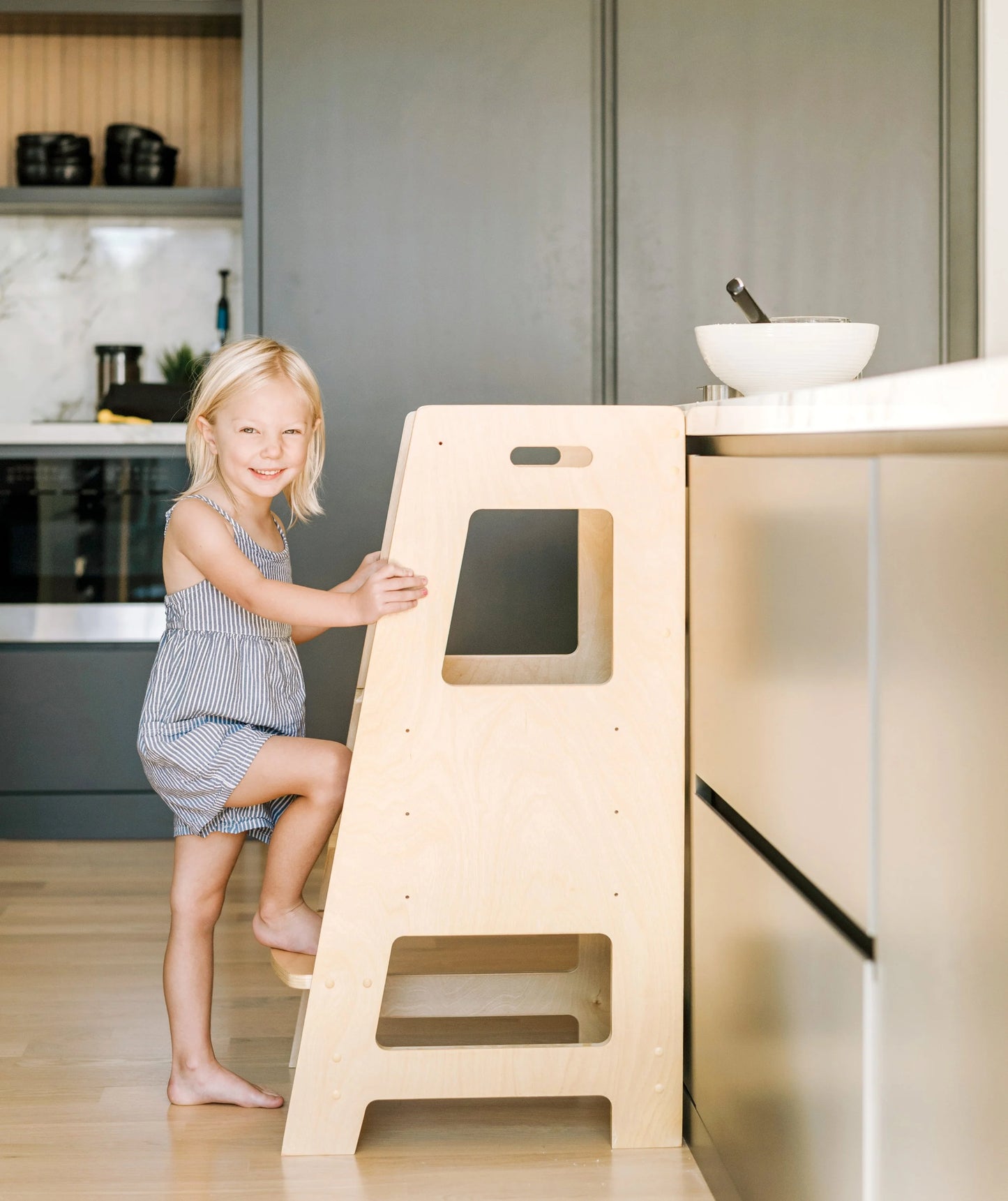Kids using a learning tower to help at the kitchen bench top