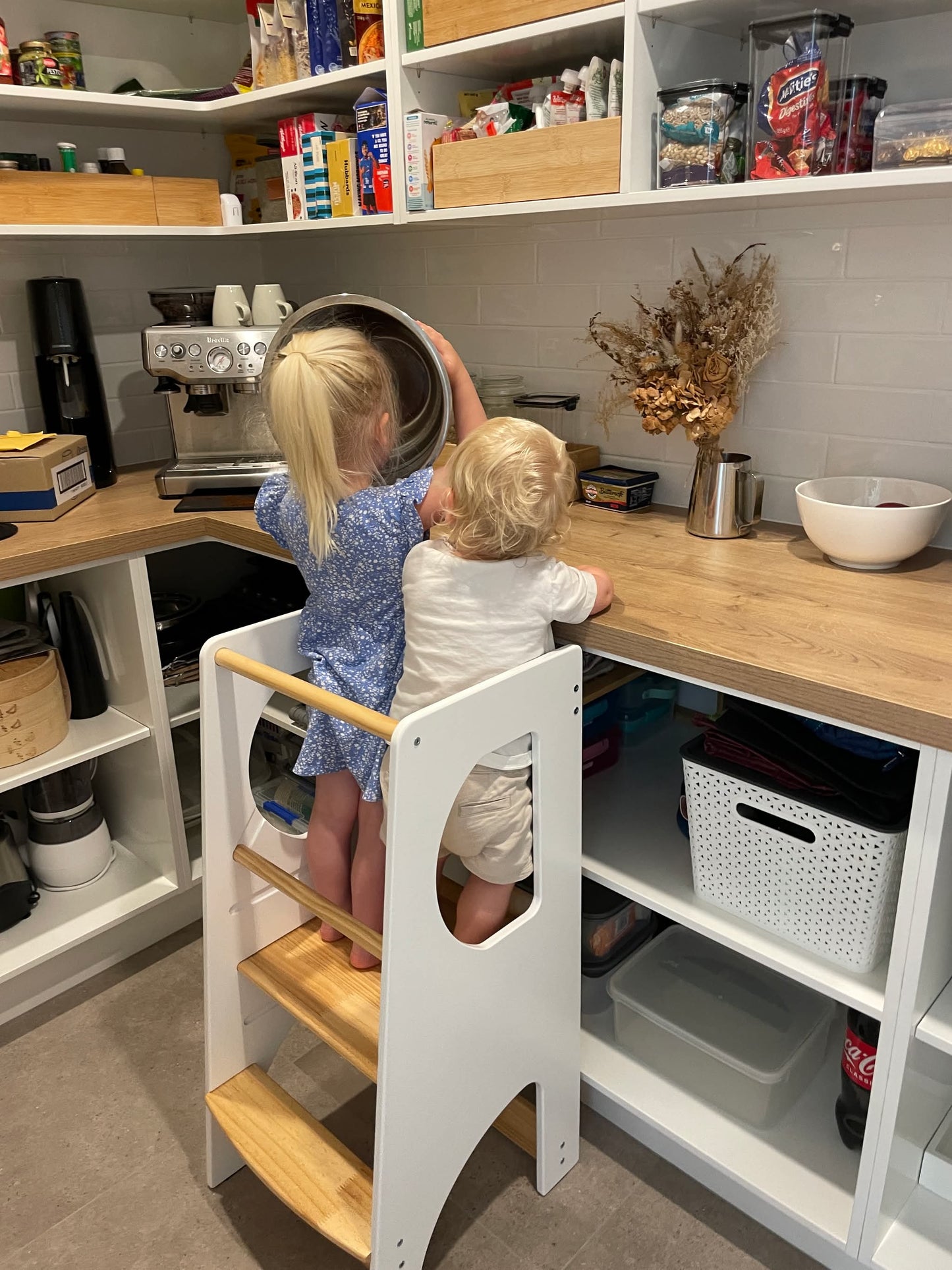 Two toddlers using our Montessori learning towers l to reach the kitchen counter.